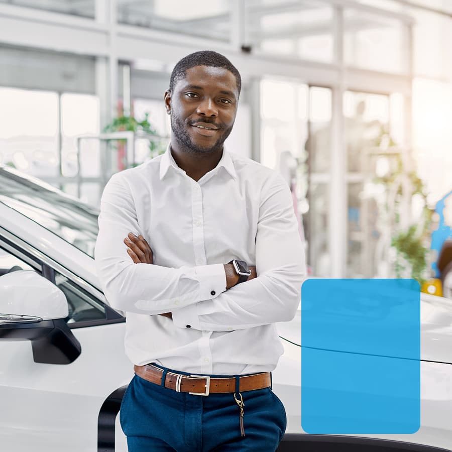 Young man standing by new car in showroom.